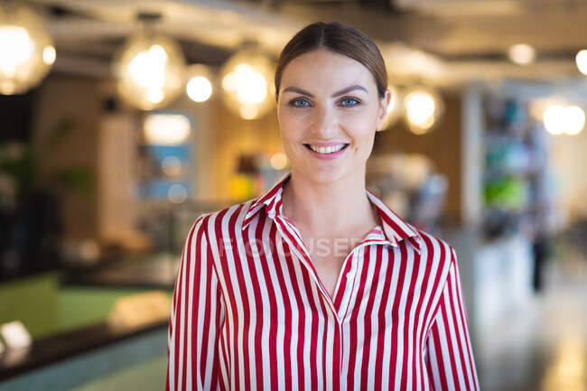 Portrait of a Caucasian businesswoman with short hair standing inside a cafe, looking at camera and smiling, wearing fashionable clothes — Stock Photo