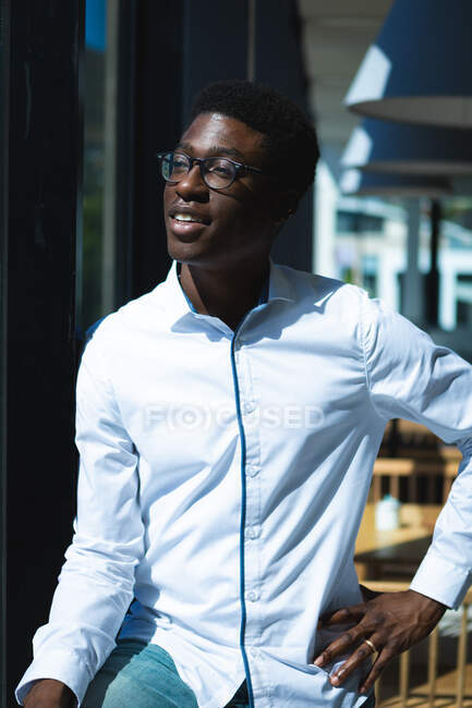 Ein afroamerikanischer Geschäftsmann mit kurzen Haaren, weißem Hemd und Brille steht in einem Café und schaut zum Fenster — Stockfoto