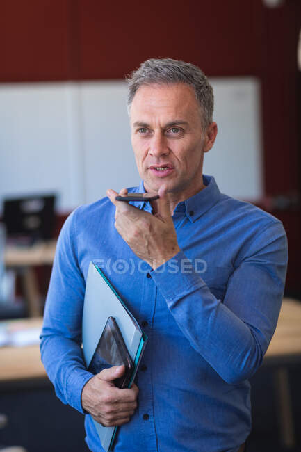 Кавказький бізнесмен у синій сорочці, який працює в сучасному офісі, стоїть і розмовляє по телефону, тримаючи табличку. — стокове фото
