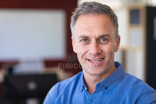 Ritratto di un uomo d'affari caucasico che indossa una camicia blu, in piedi e sorridente, lavora in un ufficio moderno, guarda la macchina fotografica — Foto stock