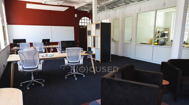 General view of an empty modern office, with desktop computers lying on tables, with a sofa in the foreground, on a sunny day — Stock Photo