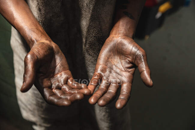 Primo piano di mani sporche di operaio afroamericano di fabbrica che indossa grembiule sporco. — Foto stock