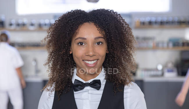 Porträt einer Kellnerin mit gemischter Rasse, die in die Kamera blickt und lächelt, während im Hintergrund Köche kochen. — Stockfoto