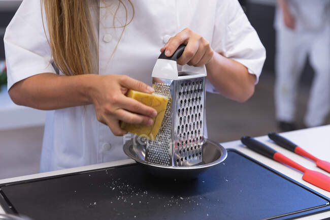Vista a metà sezione dello chef donna che grattugia il formaggio duro su una grattugia. — Foto stock