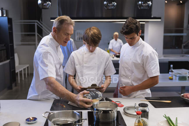 Three Caucasian male chefs standing by a table, looking at pans and pots, talking to each other. Cookery class at a restaurant kitchen. — Stock Photo