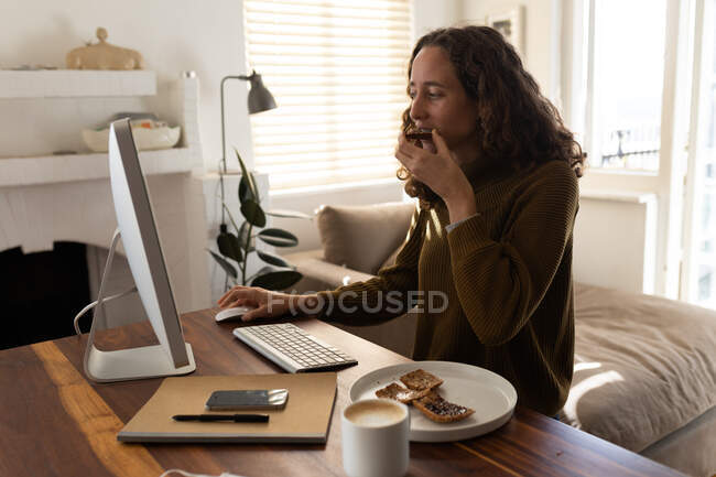 Une femme caucasienne passe du temps à la maison, utilisant son ordinateur, mangeant. Mode de vie à domicile isolement, éloignement social en quarantaine confinement pendant la coagulation du coronavirus 19 pandémie. — Photo de stock