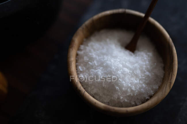 Salz in einer hölzernen Schüssel mit einem Löffel auf einem Graphittisch verschließen. Die Zubereitung von Lebensmitteln zu Hause fördert eine gesunde Lebensweise. — Stockfoto