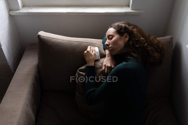 Una donna caucasica che passa del tempo a casa, sdraiata sul divano con un fazzoletto. Stile di vita a casa isolante, distanza sociale in isolamento di quarantena durante il coronavirus covid 19 pandemia. — Foto stock