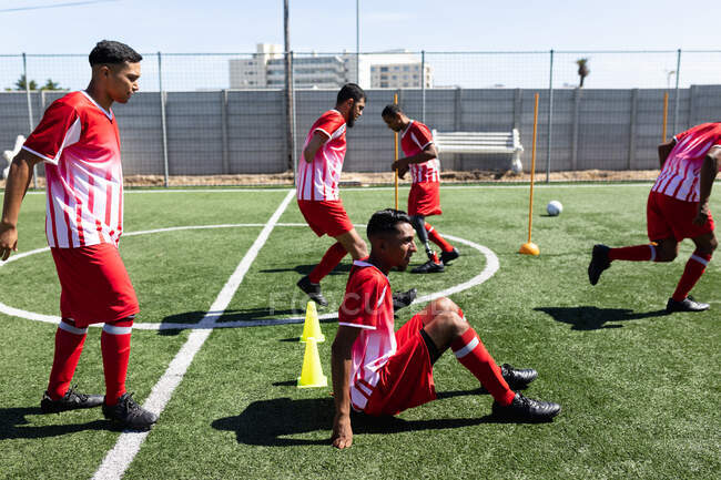 Multi ethnic team of male five a side football players wearing a team strip training at a sports field in the sun, warming up running one player with prosthetic leg one without arm. — Stock Photo
