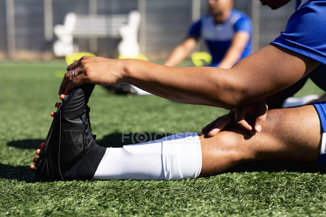 Football player wearing a team strip training at a sports field in the sun, warming up stretching his legs. — Stock Photo