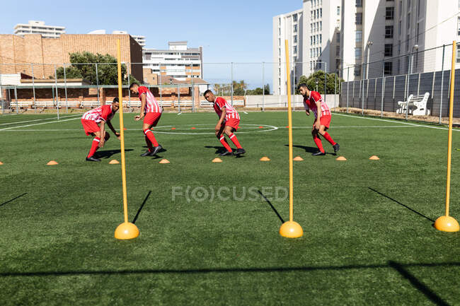 Multi ethnic team of male five a side football players wearing a team strip training at a sports field in the sun, warming up running. — Stock Photo