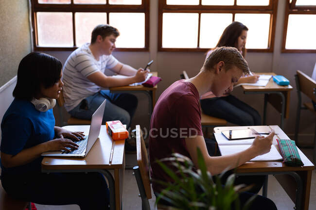 Side view of a multi-ethnic group of teenage pupils sitting at desks in class studying at school. High school education concept. — Stock Photo