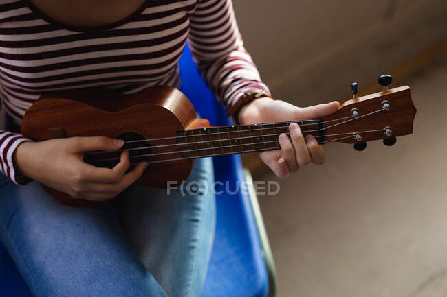 Високий кут середня частина дівчини - музиканта у смугастому светрі сидить і грає на укулеле на самоті. — стокове фото