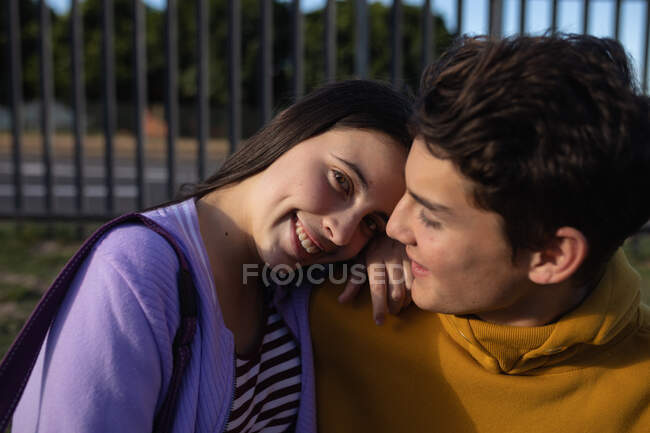 Vista frontal de cerca de una adolescente caucásica y un niño abrazando y sonriendo en sus terrenos de la escuela, la chica mirando a la cámara - foto de stock