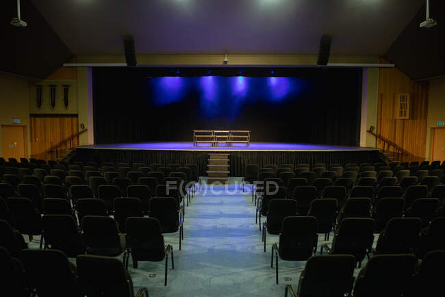Posti vuoti e palcoscenico in un teatro scolastico dal retro dell'auditorium in una scuola superiore con le luci spente — Foto stock