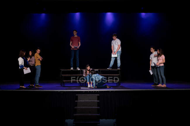 Вид спереду на багатоетнічну групу підлітків-хлопчиків і дівчат, які тримають сценарії і виступають на сцені шкільного театру під час репетицій для виступу — стокове фото