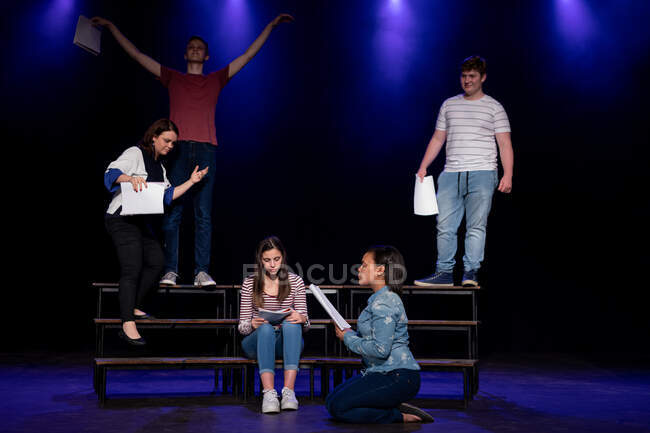 Обзор мультиэтнической группы мальчиков и девочек, держащих сценарии и выступающих на сцене школьного театра во время репетиций спектакля — стоковое фото