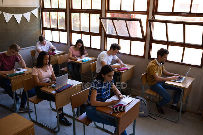 Visão de alto ângulo de um grupo multi-étnico de alunos adolescentes concentrados sentados em mesas em sala de aula estudando na escola em uma escola secundária — Fotografia de Stock