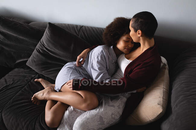Blick aus der Vogelperspektive auf ein gemischtes Paar, das es sich zu Hause im Wohnzimmer gemütlich macht, gemeinsam auf der Couch sitzt und sich am Morgen umarmt — Stockfoto