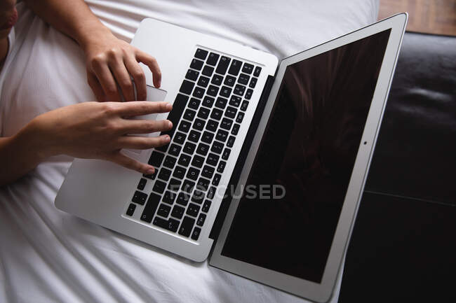 Високий кут зору рук жінки за допомогою портативного комп'ютера, що сидить у ліжку вдома — стокове фото