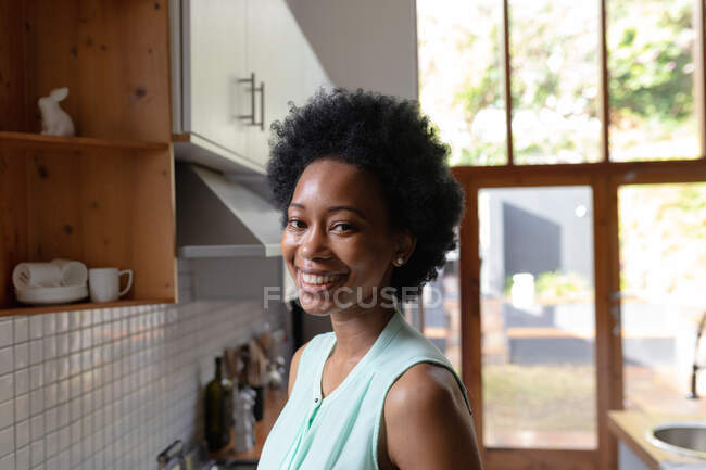 Ritratto di una attraente donna afroamericana a casa in cucina che guarda alla telecamera e sorride. Si sta godendo il suo fine settimana. — Foto stock