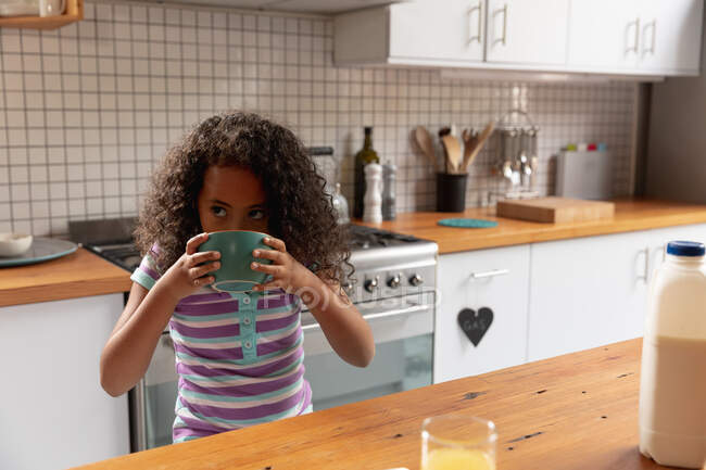 Front view of a young African American girl at home in the kitchen, sitting at a table eating breakfast cereal from the bowl — Stock Photo