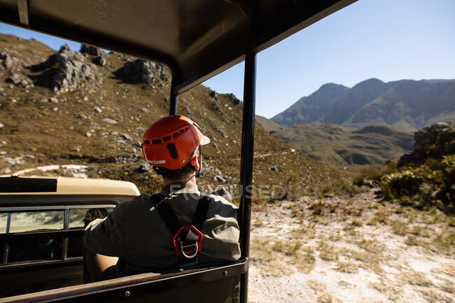 Vue arrière de l'homme caucasien profitant du temps dans la nature, dans un équipement de tyrolienne assis dans une voiture par une journée ensoleillée dans les montagnes — Photo de stock