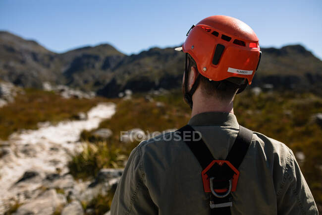 Vue arrière de l'homme caucasien profitant du temps dans la nature, portant un équipement de tyrolienne par une journée ensoleillée dans les montagnes. Fun week-end aventure vacances. — Photo de stock