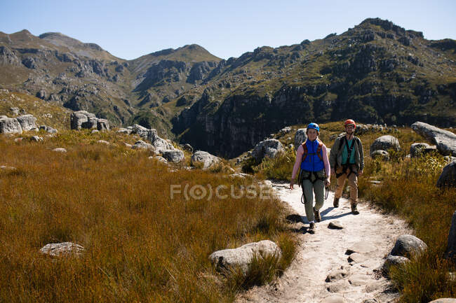 Vorderansicht eines kaukasischen Paares, das die gemeinsame Zeit in der Natur genießt, Reißverschlussausrüstung trägt und an einem sonnigen Tag in den Bergen wandert — Stockfoto
