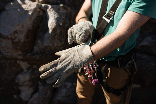 Side view mid section of man enjoying time in nature, wearing zip lining equipment, preparing to zipline, putting gloves on, on a sunny day in mountains — Stock Photo