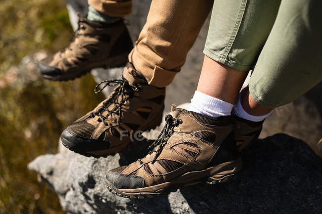 Vista lateral de cerca las piernas de la pareja juntos, disfrutando del tiempo en la naturaleza juntos, usando zapatos de senderismo, en un día soleado en las montañas - foto de stock