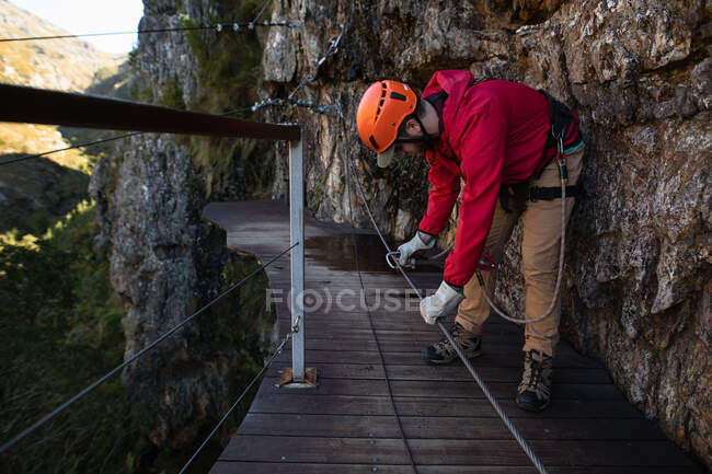 Vue latérale de l'homme caucasien profitant du temps dans la nature, portant un équipement de tyrolienne, préparant la corde à la tyrolienne par une journée ensoleillée dans les montagnes — Photo de stock