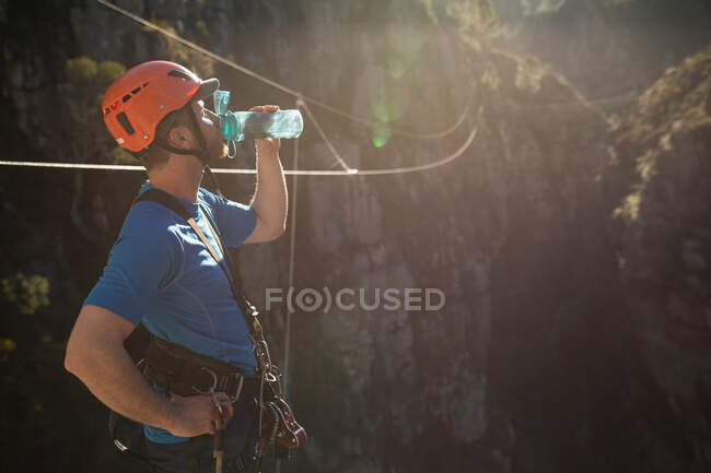 Vista laterale dell'uomo caucasico godendo del tempo in natura, indossando attrezzature zip fodera, indossando il casco, acqua potabile, in una giornata di sole in montagna — Foto stock