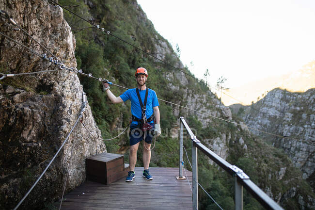 Ritratto di uomo caucasico che si gode il tempo in natura, indossa l'attrezzatura zip fodera, tiene la corda zip line, in una giornata di sole in montagna — Foto stock