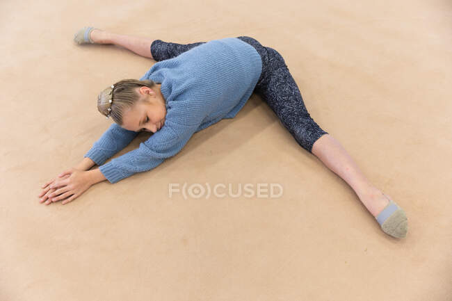 High angle side view of teenage Caucasian female gymnast practicing at the gym, stretching and warming up. — Stock Photo