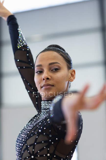 Vue de face gros plan de gymnaste adolescente mixte performant dans une salle de sport, debout avec le bras levé, portant un justaucorps noir — Photo de stock
