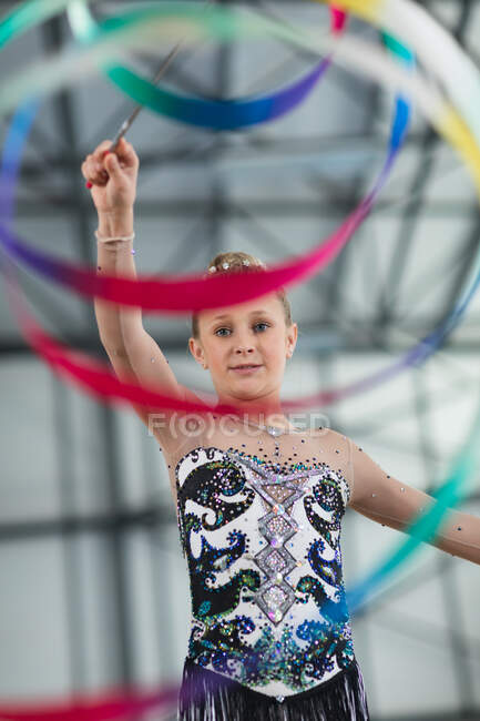 Retrato de adolescente caucasiano ginasta feminino realizando no ginásio, exercitando-se com fita, vestindo leotard multi colorido. — Fotografia de Stock