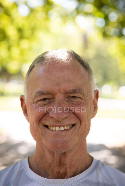 Porträt eines älteren kaukasischen Mannes, der an einem sonnigen Tag in einem Park trainiert und in die Kamera lächelt — Stockfoto