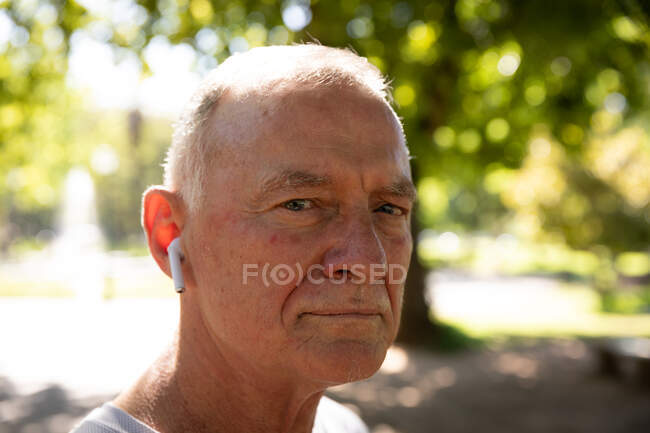Retrato close-up de um homem maduro caucasiano sênior trabalhando em um parque em um dia ensolarado, com fones de ouvido, se preparando para o treino — Fotografia de Stock