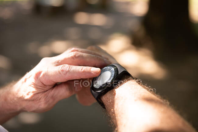 Primer plano de las manos del hombre haciendo ejercicio en un parque en un día soleado, usando smartwatch, preparándose para hacer ejercicio - foto de stock