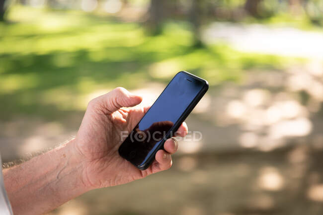 Gros plan de la main de l'homme travaillant dans un parc le jour ensoleillé, se préparant à l'entraînement, à l'aide de son smartphone — Photo de stock