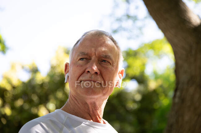 Vue de face à angle bas d'un homme caucasien âgé mature travaillant dans un parc par une journée ensoleillée, avec écouteurs allumés, se préparant à s'entraîner — Photo de stock