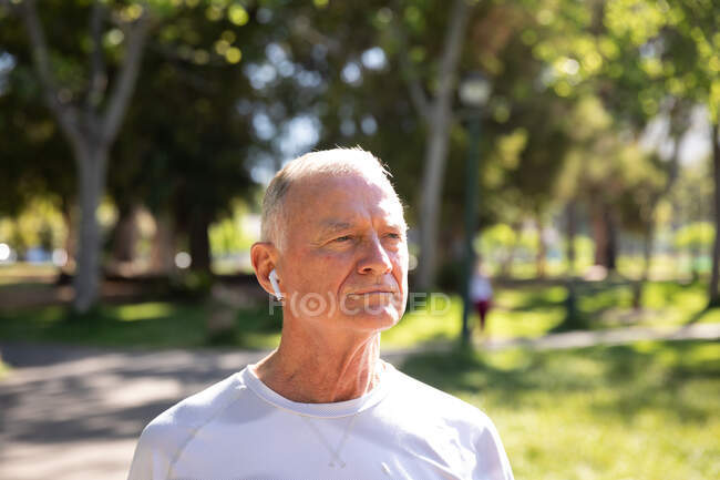 Vista frontal de um homem maduro caucasiano sênior trabalhando em um parque em um dia ensolarado, com fones de ouvido, se preparando para o treino — Fotografia de Stock