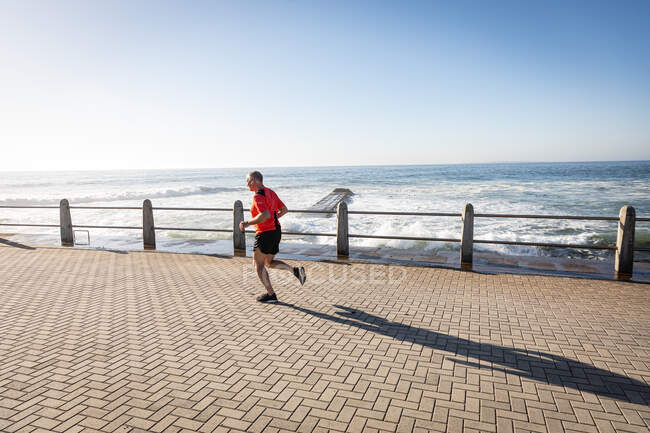 High angle side view of a mature senior Caucasian man working out on a promenade, running — Stock Photo