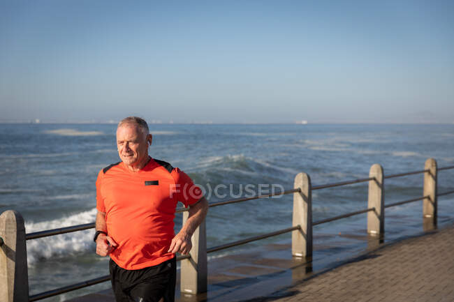 Vista frontal de un hombre caucásico mayor maduro haciendo ejercicio en un paseo marítimo, corriendo - foto de stock