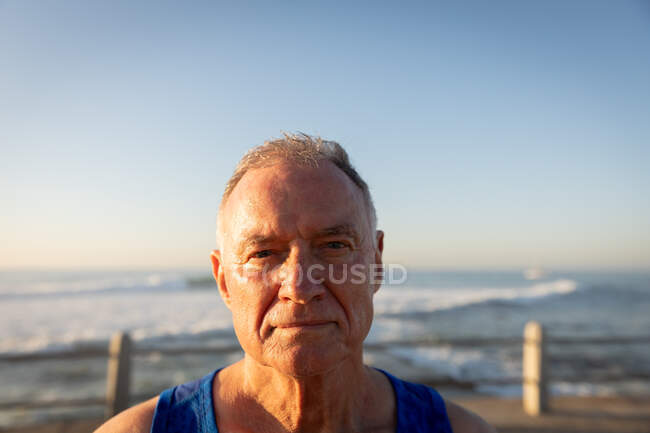 Porträt eines älteren kaukasischen Mannes, der an einem sonnigen Tag mit blauem Himmel auf einer Promenade sein Training genießt und dabei in die Kamera blickt — Stockfoto