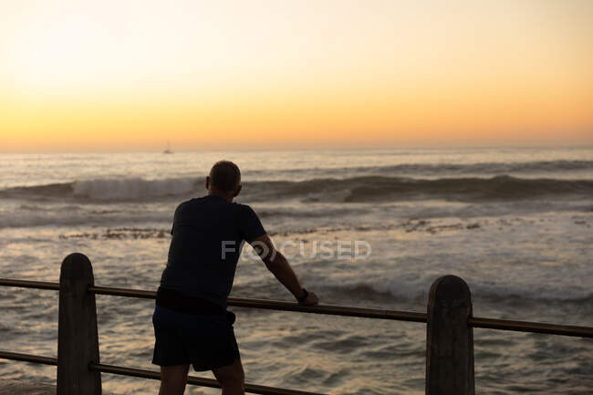 Rear view of a mature senior Caucasian man working out on a promenade, taking a break, standing, holding onto a balustrade — Stock Photo