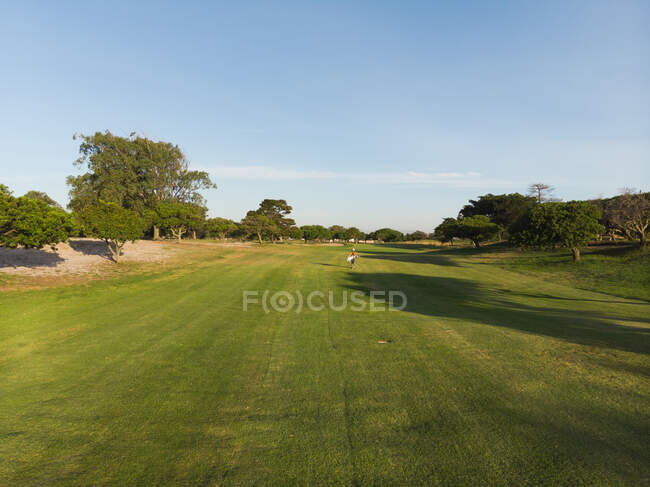 Drone shot of a golf course with golf player on sunny day with blue sky and trees next to the field — Stock Photo
