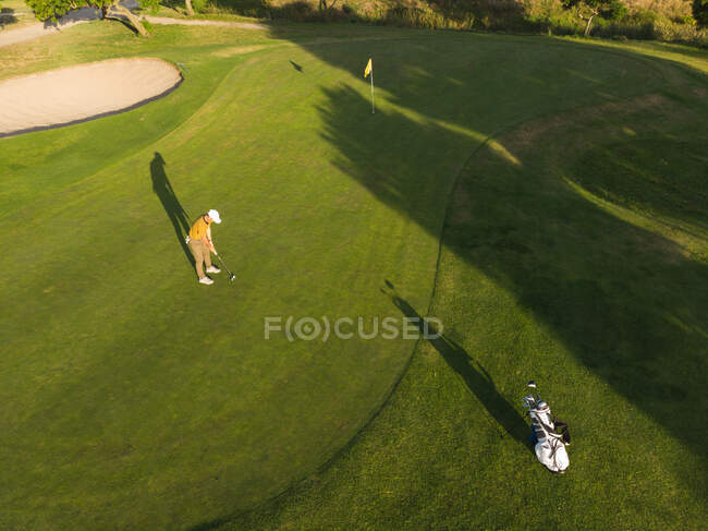 Drone tiro de un hombre jugando al golf en un campo de golf en un día soleado, concentrándose, de pie junto a una pelota antes de dar un golpe - foto de stock