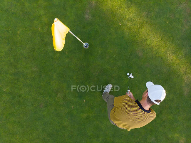 Drone shot of a man playing golf at a golf course, standing by a ball before taking a stroke into the hole — Stock Photo
